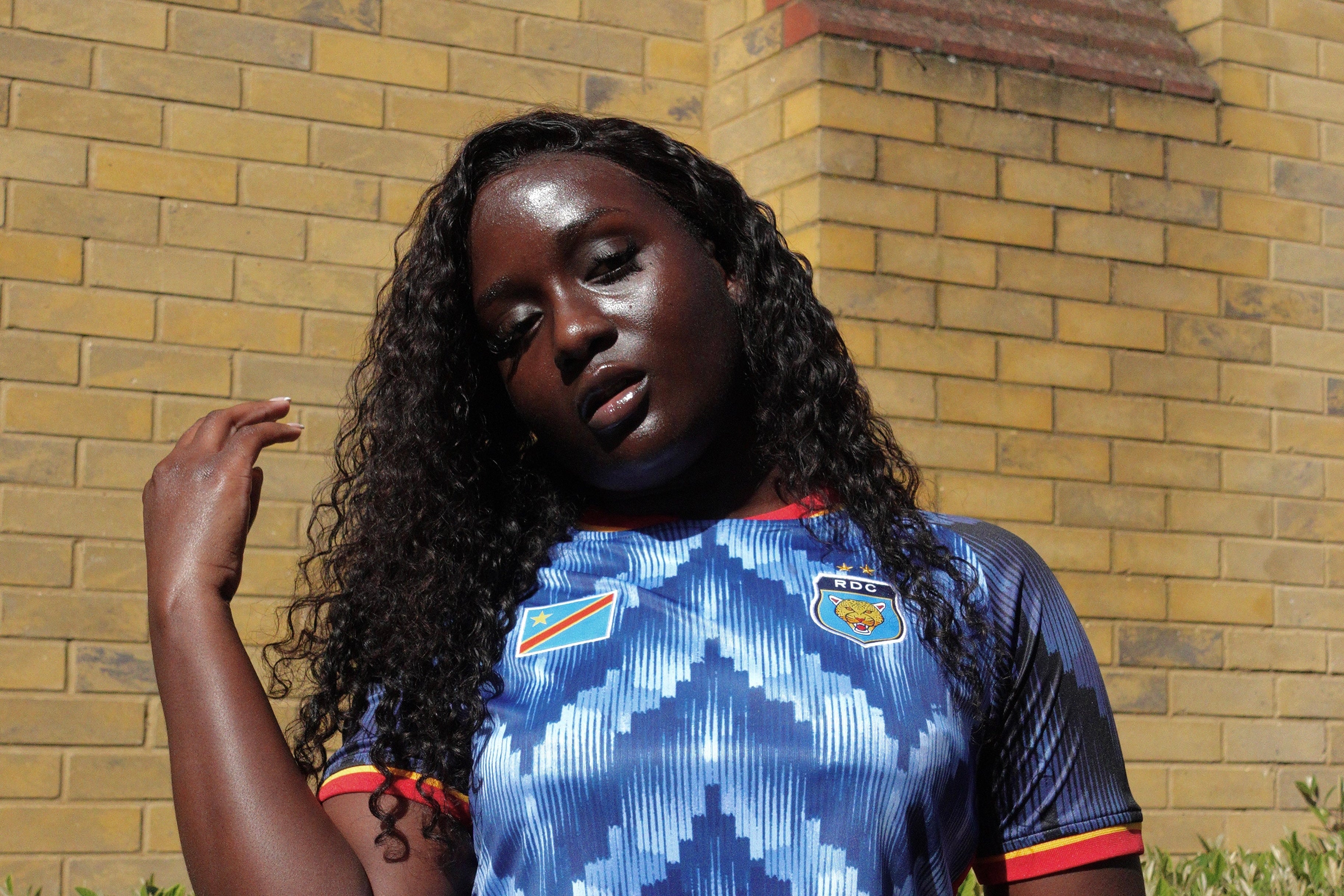 Woman wearing a blue sports jersey with logos against a brick wall.